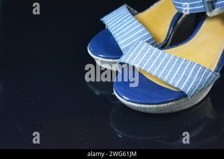 Chaussures femme élégantes et inhabituelles en cuir verni bleu véritable et tissu bleu. Sandales, sandales, chaussures de vol sont situés sur un noir brillant. Banque D'Images