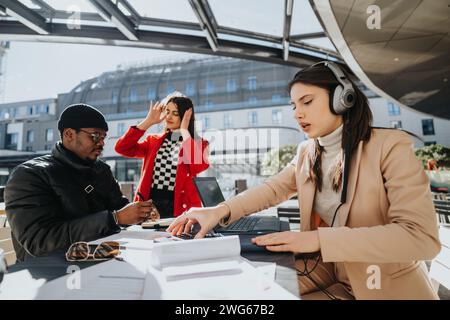 Un groupe multiculturel de jeunes engagés dans une discussion, travaillant sur un ordinateur portable et portant des écouteurs, dans un cadre urbain extérieur. Banque D'Images