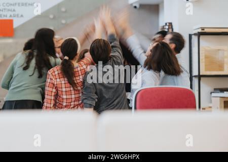 Groupe dynamique de collègues donnant high-fives dans une célébration joyeuse de la réussite commerciale dans un environnement de bureau contemporain. Banque D'Images