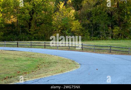 Une route pavée paisible tourne autour d'une petite prairie bordée d'arbres. La clôture en bois rustique semble offrir une invitation bienvenue à la tranquillité dans Arkansa Banque D'Images