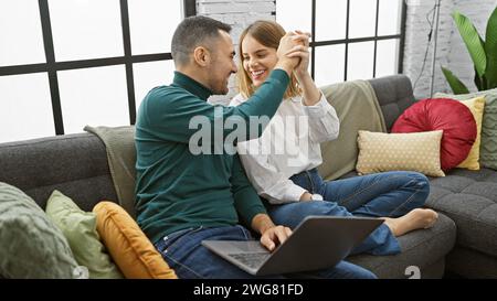 Un couple aimant profite du temps de qualité ensemble dans leur salon confortable avec un ordinateur portable, entouré d'oreillers colorés. Banque D'Images