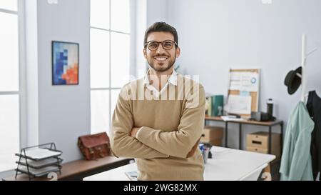 Beau jeune homme avec les bras croisés debout avec confiance dans un intérieur de bureau moderne bien éclairé. Banque D'Images