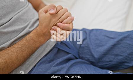 Gros plan sur les mains serrées d'un jeune homme reposant sur un lit dans une chambre intérieure reflétant l'anticipation ou l'inquiétude. Banque D'Images