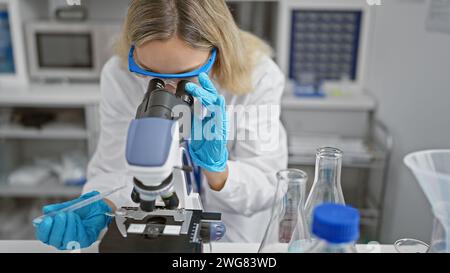 Une femme scientifique focalisée utilise un microscope dans un cadre de laboratoire, indiquant la recherche et les soins de santé. Banque D'Images