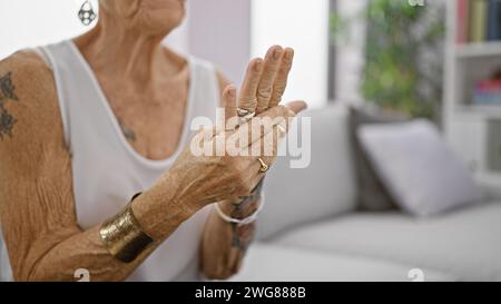 Femme âgée aux cheveux gris souffrant de douleurs intenses aux mains, assise dans le canapé du salon à la maison, femme âgée avec les cheveux courts semblant blessée, arthrose Banque D'Images