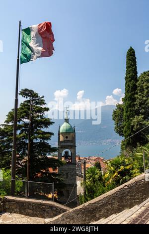 Le drapeau italien flotte au-dessus du clocher de l'église de Saints Nazaro et Celso avec le lac de Côme au-delà à Bellano, Lombardie, Italie. Banque D'Images