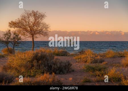 La vue du coucher du soleil sur le lac Issyk-Koul au Kirghizistan, une destination touristique populaire, avec l'eau bleue et les montagnes Tian-Shan à l'horizon. Banque D'Images