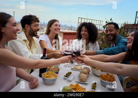 Groupe riant de jeunes amis divers profitant d'un déjeuner ensemble célébrant la fête de toasting sur le toit. Banque D'Images