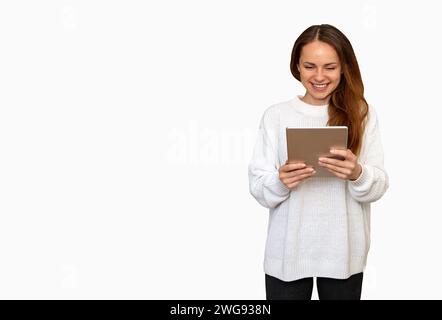 Isolée jeune femme brune avec les cheveux longs portant un pull blanc à l'aide d'une tablette numérique et souriant. Banque D'Images