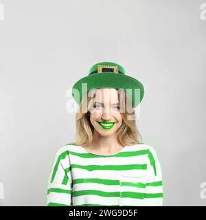 Prog Fête de Patrick. Jolie femme avec des lèvres vertes en chapeau de leprechaun sur fond gris clair Banque D'Images