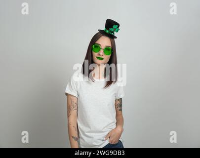 Prog Fête de Patrick. Jolie femme en chapeau leprechaun et lunettes de soleil vertes sur fond gris clair Banque D'Images