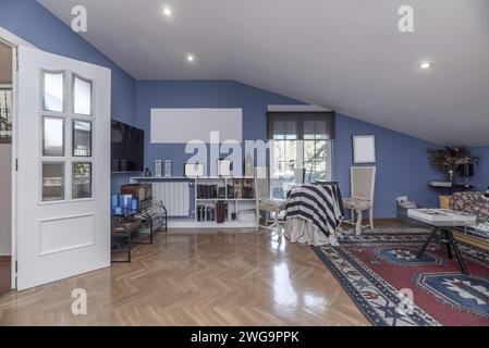 salon d'une maison avec murs peints en bleu, menuiserie blanche sur les portes, plafonds en pente, parquet en chêne et tapis couvrant la moitié Banque D'Images