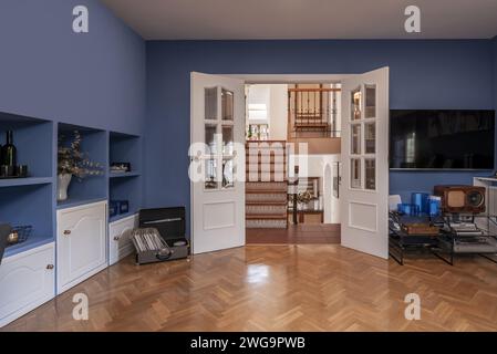 Salle de séjour mansardée, parquet en chêne, murs peints en bleu, armoire encastrée et menuiserie en bois blanc Banque D'Images