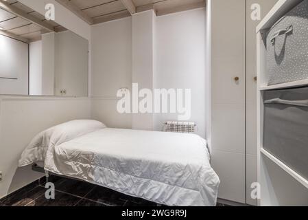 Une petite chambre aux murs blancs avec plafond à caissons en bois, un lit simple avec couette blanche et de grands miroirs accrochés au mur Banque D'Images