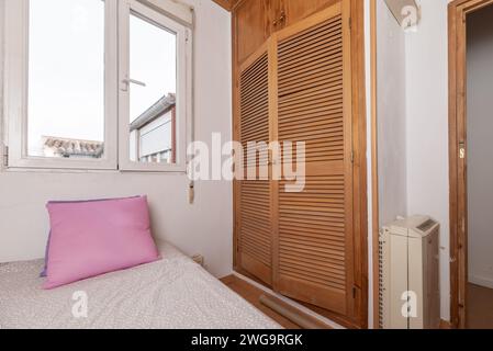 Une chambre avec une armoire intégrée avec des portes en bois de style vénitien et un lit avec des coussins Banque D'Images