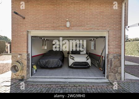Un garage d'une maison unifamiliale avec deux voitures garées, l'une d'entre elles recouverte d'une bâche Banque D'Images