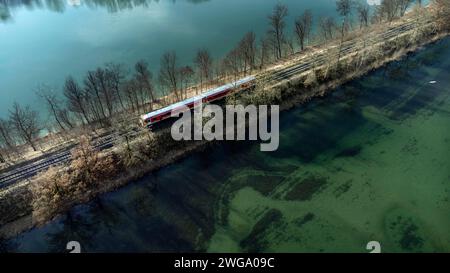 Un chemin de fer local rouge circule sur un remblai entre deux eaux turquoise, tir par drone, haute-Bavière, Bavière, Allemagne Banque D'Images