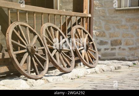 Trois vieilles roues en bois pour charrettes à chevaux appuyées contre un mur en bois en perspective Banque D'Images