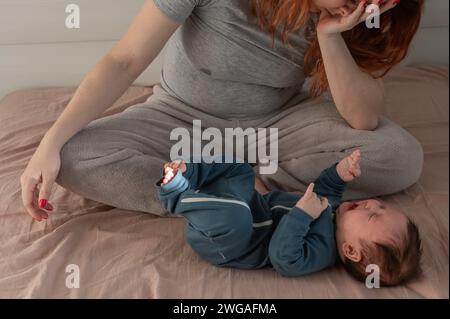 Une femme caucasienne est assise sur un lit à côté d'un bébé qui pleure. Dépression du post-partum. Banque D'Images