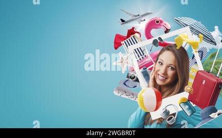 Jeune femme joyeuse dans un cadre photo instantané entouré d'accessoires de plage et d'articles de voyage, elle rêve de ses vacances d'été Banque D'Images