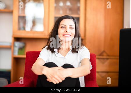 Portrait d'une femme souriante assise dans un fauteuil serrant ses genoux Banque D'Images