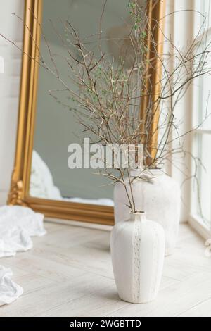Gros plan de branches décoratives dans des vases en céramique sur le sol à côté d'un miroir de longueur de sol dans la chambre Banque D'Images