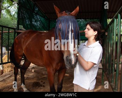 Adolescente dans une écurie toilettant son cheval, New Delhi, Inde Banque D'Images