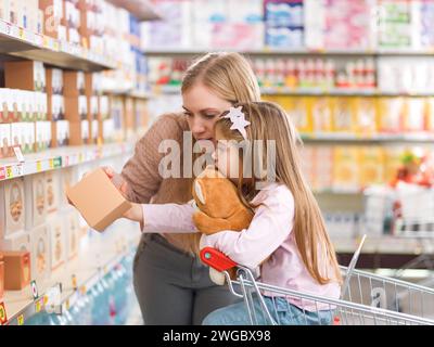 Mignon famille heureuse faisant des courses au supermarché : une mère et sa fille choisissent l'épicerie sur l'étagère du magasin Banque D'Images