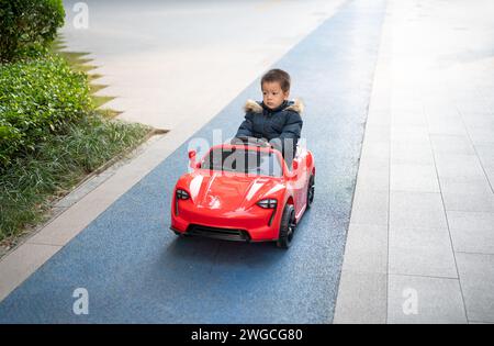 Un jeune enfant multiracial navigue joyeusement sur la piste de course du quartier dans une voiture de sport rouge, enfilant un grand sourire alors qu'ils prennent le contrôle du Banque D'Images