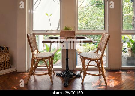 Table à manger en bois avec chaise en rotin et couverts à côté de la fenêtre du restaurant Banque D'Images