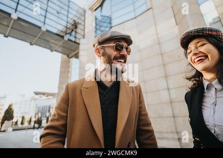 Deux jeunes entrepreneurs joyeux s’engagent dans une discussion collaborative en dehors de l’architecture urbaine moderne, dépeignant le travail d’équipe et la dynamique du travail à distance. Banque D'Images