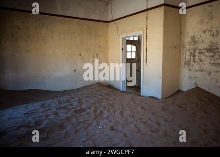 Une chambre abandonnée avec un plancher de sable spacieux adjacent à une porte ouverte Banque D'Images