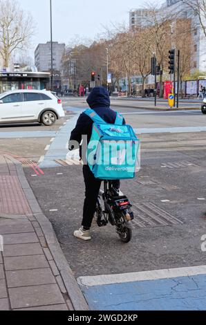 Vue arrière d'un employé de Deliveroo sur un vélo électrique attendant aux feux de circulation sur la Whitechapel High Street, Londres Angleterre Royaume-Uni Banque D'Images