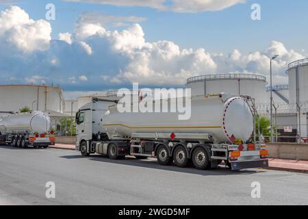 Les camions avec des remorques de réservoirs de carburant blancs sont garés à côté d'un énorme baril de stockage de pétrole Banque D'Images