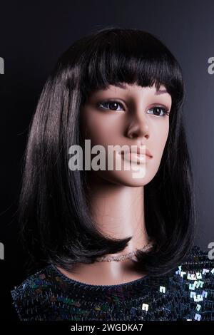 Mannequin femme en plastique avec de longs cheveux noirs et paillettes haut posant sur un fond noir avec effet de lumière de cheveux Banque D'Images