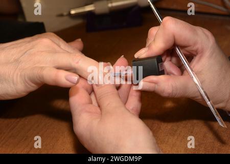 Le manucure tient les doigts du client dans sa main et utilise un pinceau pour appliquer du vernis coloré sur les ongles. Banque D'Images