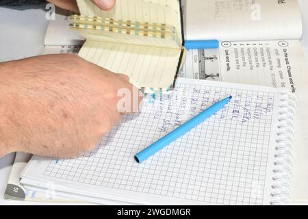 Un homme est assis à une table avec un cahier, un livre et un stylo dessus. L'homme tient un bloc-notes dans ses mains. Banque D'Images