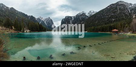 Vue panoramique sur le lac alpin d'eau turquoise Lago di Dobbiaco avec restaurant dans les montagnes Dolomiti, Cortina dAmpezzo, Italie sur le jour de printemps sombre Banque D'Images