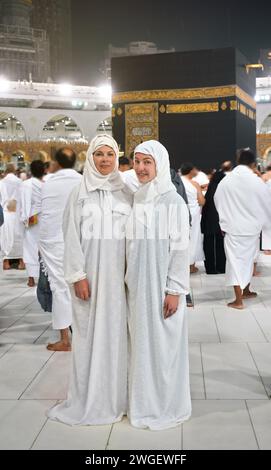 Deux femmes caucasiennes en longue robe blanche debout devant la Kaaba à la Mecque pendant leur pèlerinage. Tous les autres visages sont flous. À partir de 2023 vi Banque D'Images