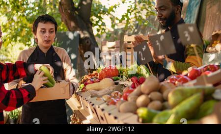 Homme senior et jeune femme achetant des produits bio biologiques, visitant le stand de marché des agriculteurs locaux. Des vendeurs souriants saluant les clients et vendant des fruits et légumes cultivés sur place de la ferme. Banque D'Images