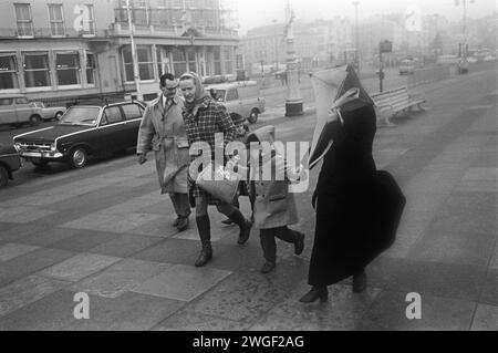 Sortie familiale des années 1960 Brighton promenade UK. La pluie et un vent éclatant se produisent une promenade familiale le dimanche matin le long de la promenade du front de mer à Brighton pendant le mauvais temps traditionnel anglais en bord de mer. Brighton, East Sussex, Angleterre 1969 HOMER SYKES Banque D'Images