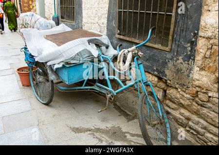 Un tricycle altéré est garé à côté d'un mur de pierre sur la place Barkhor. Banque D'Images