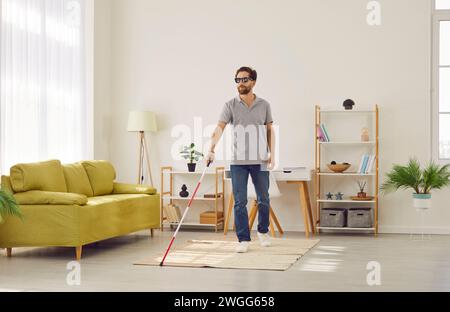 Liez un jeune homme handicapé dans des vêtements décontractés avec une canne marchant dans le salon à la maison. Banque D'Images