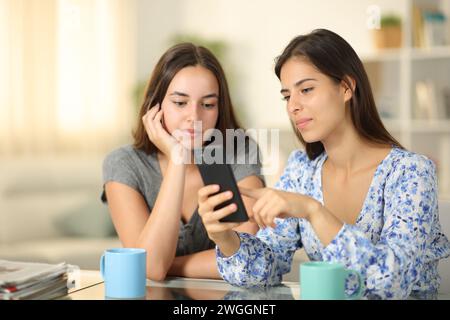 Amis sérieux vérifiant le contenu du téléphone à la maison Banque D'Images