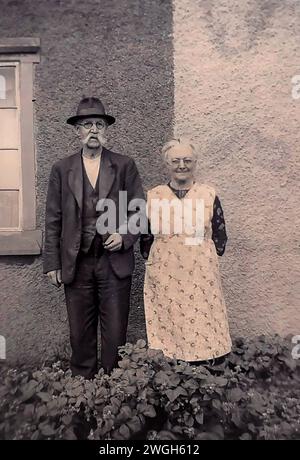 Tiré du négatif original (donc des imperfections peuvent être présentes), une photo d'un couple debout dans leur jardin au début des années 1940 L'homme a une moustache en guidon et porte un chapeau Trilby. La dame porte un long Housecoat (pinafore). Banque D'Images