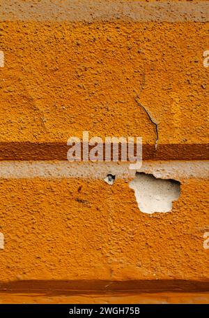 Close-up d'un mur orange vif à Budapest avec une ligne horizontale, une surface craquelée et du plâtre écaillé révélant une couche blanche en dessous Banque D'Images