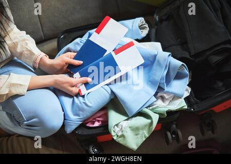 Concentrez-vous sur le passeport et le ticking. Femme tenant des attributs de voyage au-dessus de la valise avec des vêtements. Préparation du voyage Banque D'Images