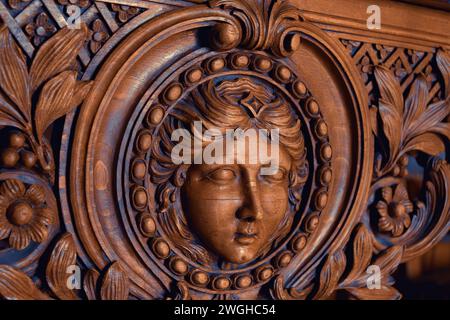 Élégante sculpture en bois du visage d'une femme (peut-être Marianne, symbole de la France) avec des motifs floraux complexes sur des meubles vintage. Paris, France. Banque D'Images