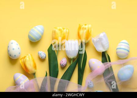 Joyeuses Pâques. Oeufs colorés peints de pâques et tulipes blanches et jaunes sur fond jaune Banque D'Images