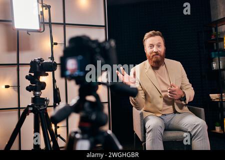 homme joyeux avec les cheveux roux et la barbe dans une tenue élégante parlant activement pendant podcast en studio Banque D'Images
